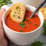 A bowl of creamy tomato soup with a baguette slice.