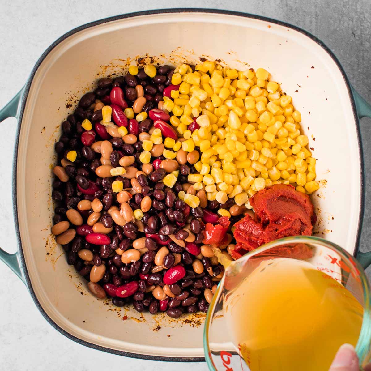 Beans, corn, tomato paste, and more ingredients added into the pot.