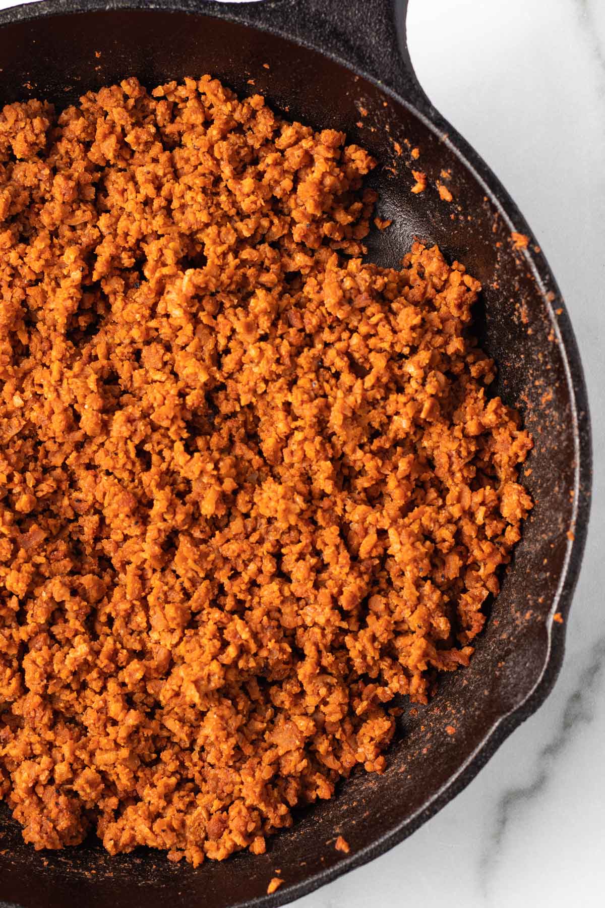 Vegan ground beef substitute cooking in a cast iron pan.